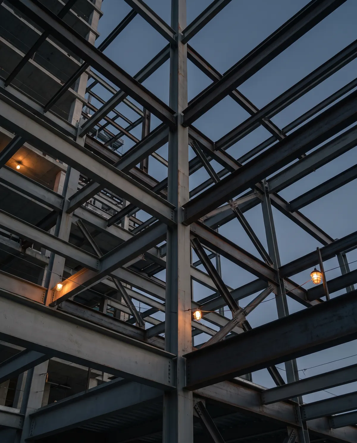 Estructura de acero en montaje vista desde abajo al atardecer: columnas, vigas y arriostres